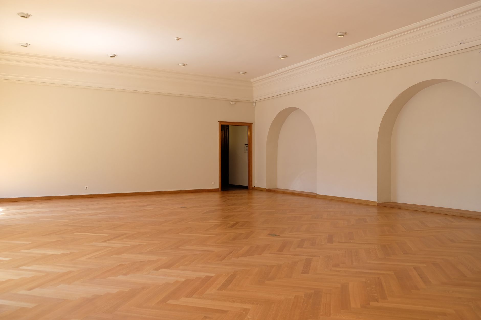 A large empty room with elegant wooden flooring, arches, and natural lighting